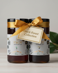 Two jars of Troy Raw Greek honey with a gold ribbon and label on a wooden surface.