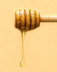 Honey dipper with Troy Greek Raw Honey dripping on a beige backgroundney
