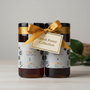 Two jars of Troy Greek Raw Honey with a gold ribbon and label on a wooden surface.